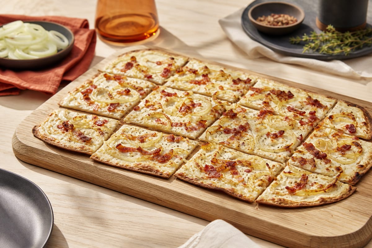 Knuspriger Flammkuchen mit Zwiebeln und Speck auf einem Holzbrett